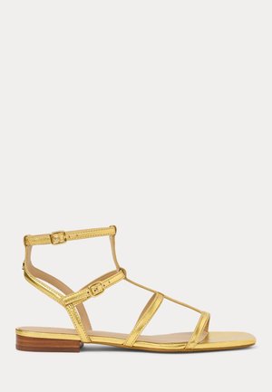 Gold metallic flat sandals with multiple strappy designs, adjustable buckles, and a low wooden heel. Smooth texture and open toe.