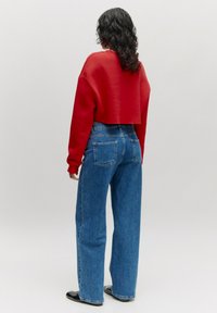 Ingekorte rode sweatshirt en high-waisted blauwe jeans. Zachte textuur, relaxte pasvorm. Eenvoudig ontwerp met achterzakken op de jeans en effen kleuren.