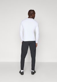 Weißes langärmliges Oberteil kombiniert mit schwarzen Sporthosen. Glatter Stoff, figurbetontes Design. Schwarze Schuhe mit sichtbaren weißen Socken.