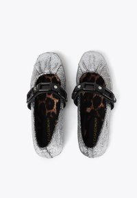 Srebrne metaliczne baleriny o teksturowanym wykończeniu, zaokrąglonym nosku i czarnym pasku z dekoracyjnymi elementami. Wnętrze z printem w panterkę.