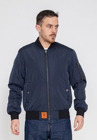 Marine bomberjack met een ritssluiting aan de voorkant, ribbelkraag en -manchetten, zijzakken en een oranje label aan de zoom. Glad, lichtgewicht stof.
