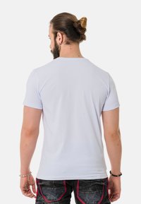 Weißes T-Shirt mit kurzen Ärmeln, Rundhalsausschnitt, glatte Textur. Getragen mit dunklen Jeans mit roten Akzenten und Gesäßtaschen.