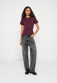 Μπορντό κοντομάνικη μπλούζα με διακριτικό λογότυπο στο στήθος, συνδυασμένη με γκρι τζιν ψηλόμεσα, άνετης γραμμής και μαύρα παπούτσια.