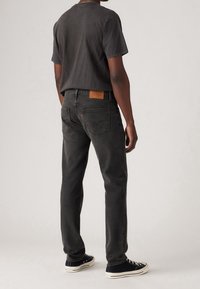 Svarta jeans med raka ben, kombinerade med en matchande svart t-shirt. Jeansen har en brun läderpatch och bärs med svarta sneakers.