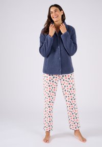 Marineblauwe fuzzy jas met kraag over crèmekleurige broek met kleurrijke hartpatronen. Zachte textuur, ontspannen pasvorm en knoopsluiting op de jas.