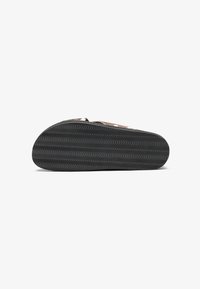 Semelle en caoutchouc noir avec un motif en vagues, présentant un design plat et des détails de traction, avec une tige en tissu marron clair et des accents texturés.