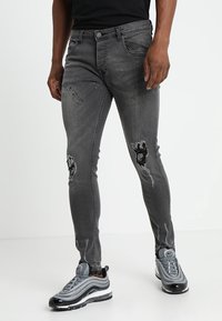 Jeans ajustados grises con detalles desgastados, incluyendo desgarros en las rodillas. Hechos de denim con un ligero estiramiento para mayor comodidad.