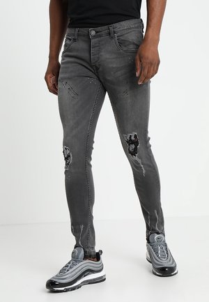 Jean skinny gris avec des détails déchirés, y compris des déchirures au niveau des genoux. Fabriqué en denim avec un léger stretch pour le confort.
