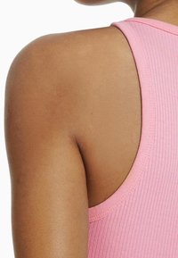 Débardeur côtelé rose avec un col arrondi, présentant une texture lisse et des bretelles étroites, mettant en valeur les épaules et la peau dénudées.