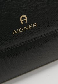 Czarny skórzany portfel o teksturowanej powierzchni. Posiada złote wytłoczone logo oraz obszycie. Kompaktowy prostokątny kształt.