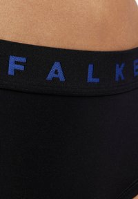 Schwarzer elastischer Bund mit blauer "FALKE"-Beschriftung, strukturierte Oberfläche, glattes Material, Nahaufnahme des Bundes und des Hauttons.