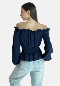 Marineblaues, schulterfreies Oberteil mit gerafftem Ausschnitt, geraffter Taille und langen Ärmeln, kombiniert mit hellblauen, hoch taillierten Jeans.