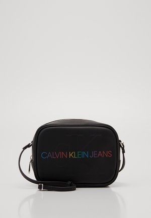 Sac rectangulaire noir avec une texture lisse, arborant un texte en dégradé arc-en-ciel "CALVIN KLEIN JEANS" à l'avant et une bandoulière réglable.