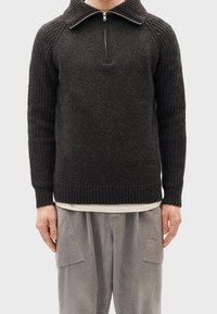Pullover in misto lana grigio scuro; texture a costine, colletto half-zip e polsini aderenti. Abbinato a pantaloni in velluto a coste grigio chiaro.