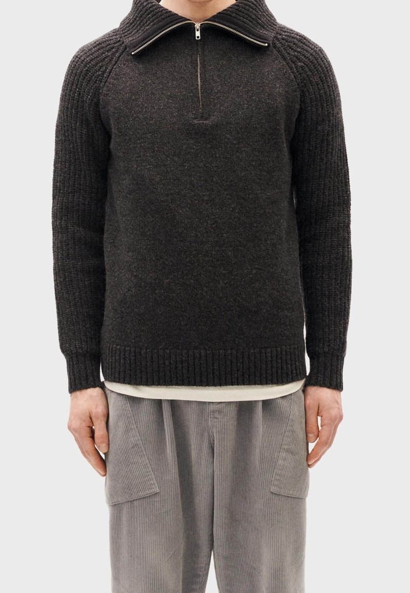 Pullover in misto lana grigio scuro; texture a costine, colletto half-zip e polsini aderenti. Abbinato a pantaloni in velluto a coste grigio chiaro.