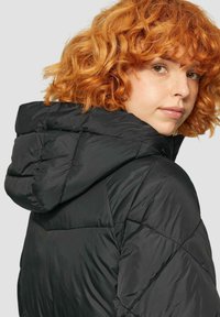 Zwarte pufferjack met kap, met een gewatteerde textuur, een gladde afwerking en zichtbare naden en stiksels. Ontworpen voor warmte en comfort.