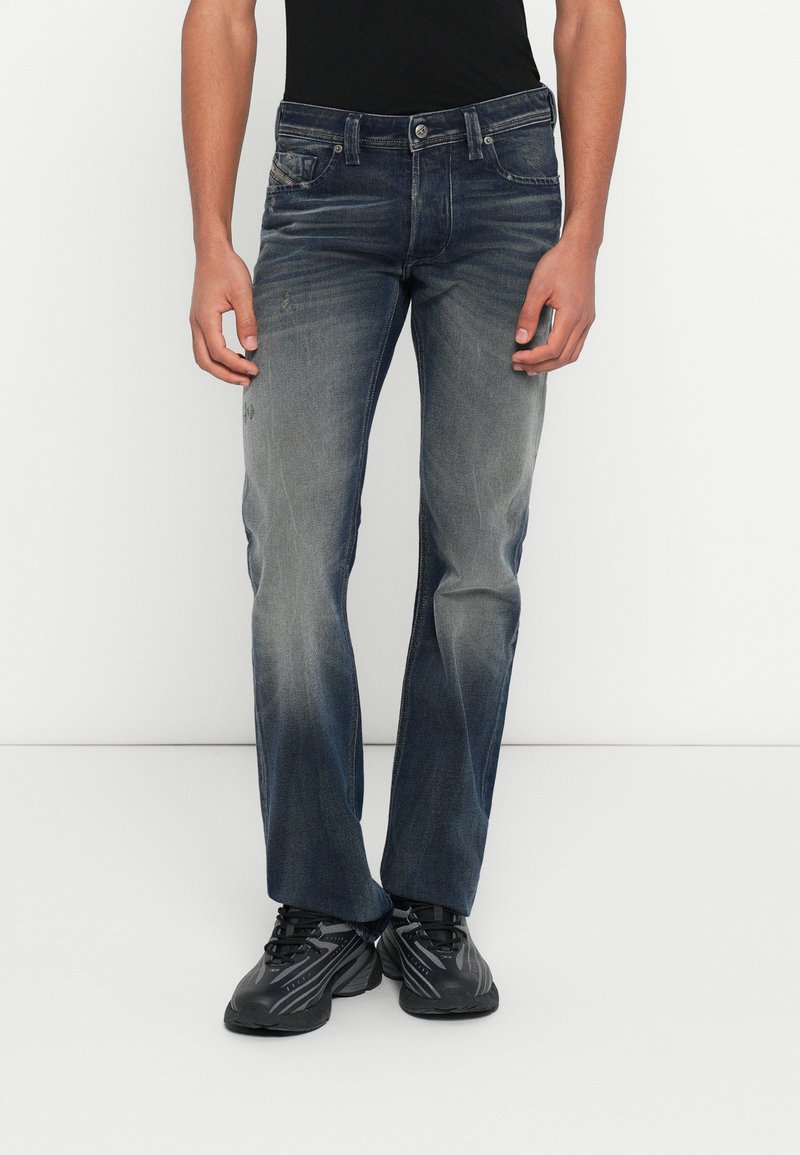 Ξεθωριασμένο μπλε τζιν με ίσια γραμμή, μπροστινές τσέπες και ελαφρά φθαρμένη όψη. Συνδυάζεται με μαύρα αθλητικά παπούτσια.