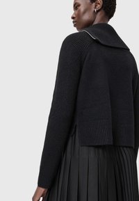 Μαύρο πλεκτό πουλόβερ με ριγέ υφή, φαρδύ γιακά και πλαϊνές σχισμές, συνδυασμένο με πλισέ μαύρη φούστα.