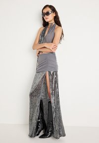 Vestido halter metálico con tela gris y detalles de lentejuelas, que presenta una apertura hasta el muslo y se combina con botas negras hasta la rodilla.