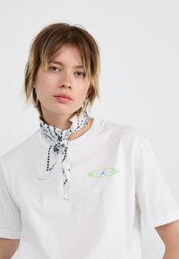 Weißes Baumwoll-T-Shirt mit einem bunten ovalen Grafikdesign auf der Brust. Dazu ein gemusterter Schal um den Hals. Einfaches Design.