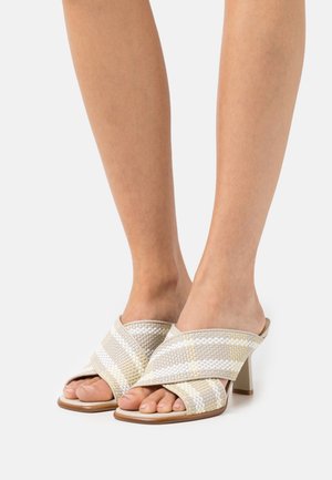 Geweven open teen muiltjes in beige met gouden accenten, met een cross-strap ontwerp en een blokhak voor ondersteuning. Zacht, textuurmateriaal.