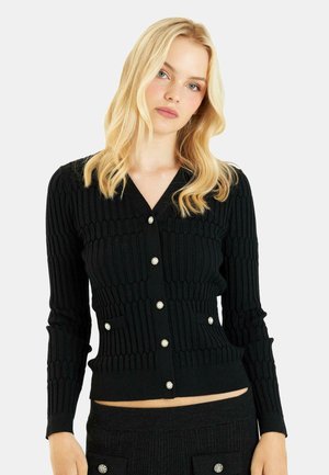 Black ribbed cardigan with a deep V-neck, long sleeves, and pearl-button closures. Features two pockets at the waist for added detail.