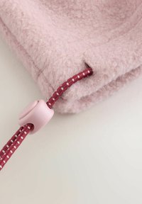 Puha rózsaszín bolyhos anyag texturált felülettel. Bordó zsinórral és rózsaszín toggle-lal rendelkezik. A felső széle közeli képe.