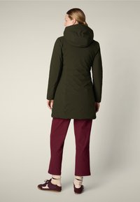 Abrigo capucha verde oscuro con un diseño ajustado, detalles de costura en relieve, combinado con pantalones burdeos y zapatillas multicolor.