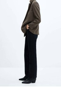 Hnědý texturovaný blazer s klopami, spárovaný s černými rovnými džínami a černými špičatými kotníkovými botami. Čistý, minimalistický design.