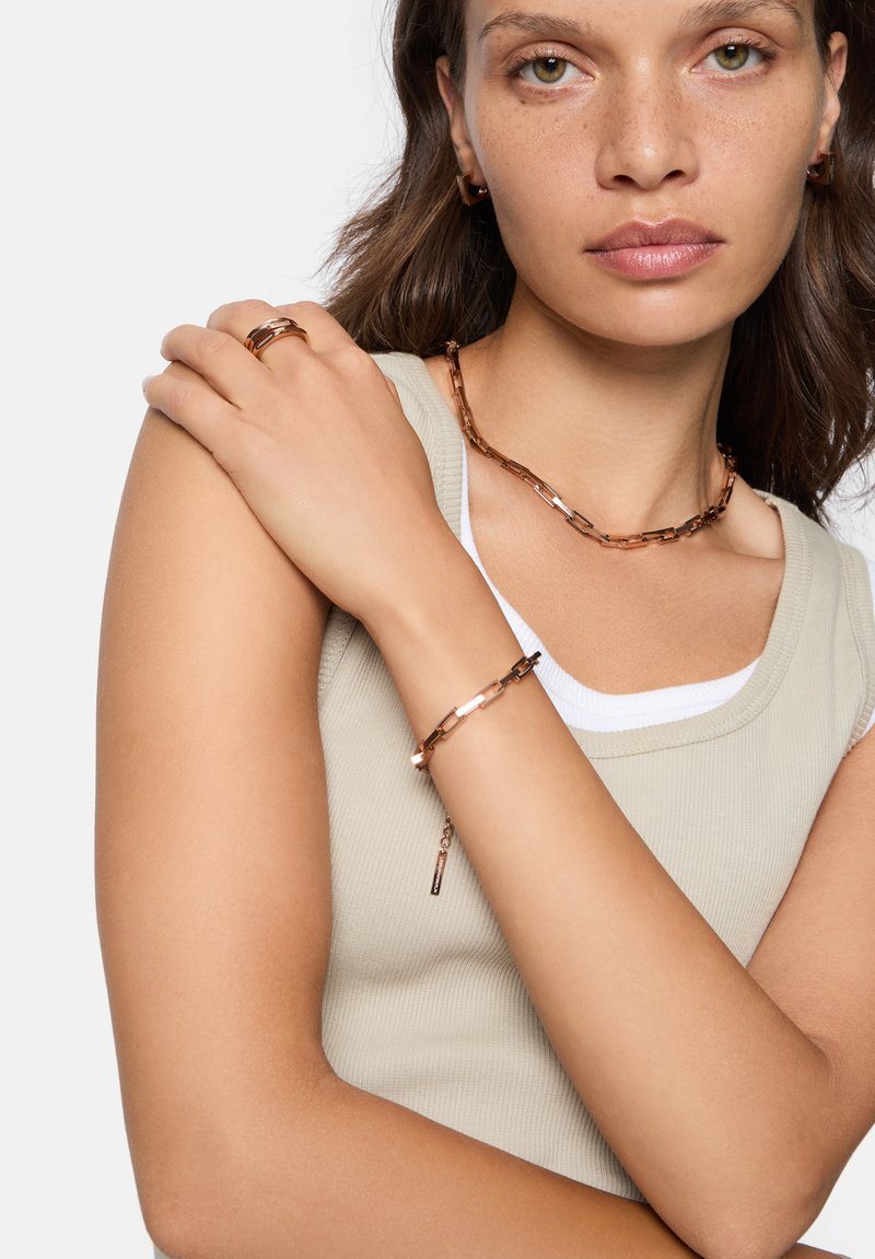 Roséguld kedja och armband med vinklade länkar, bar på en ljusbeige rutad linne topp, med en elegant metallisk detalj.