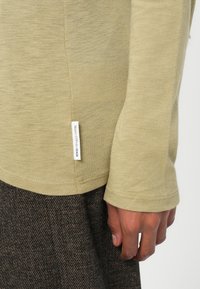 Lange mouwen licht khaki shirt van zachte stof, met een zijlabel en ribgebreide manchetten, gedragen met een textuur bruin patroon onderstuk.