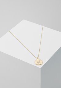 Goldene Anhängerkette mit runder Charm, die ein kleines graviertes Sternenkonstellationsdesign zeigt, aufgehängt an einer feinen Kette.