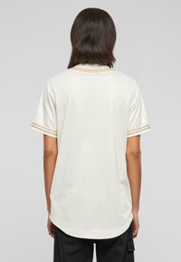 Camicetta a maniche corte color crema con sottili righe verticali, caratterizzata da accenti a righe a contrasto sulle maniche e un orlo curvo.