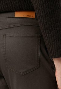 Czarne dżinsy z denimu z charakterystyczną tylną kieszenią, uzupełnioną brązową skórzaną metką z napisem "COMMA", prezentującą estetyczne detale szycia.