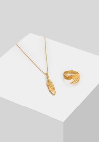 Gouden ketting met een bladhanger en een bijpassende ring met bladpatroon, beide met ingewikkelde details en een gepolijste afwerking.