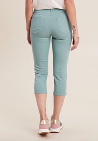 Jeans cropped di un blu teal chiaro con un design aderente, due tasche posteriori e una trama liscia, abbinati a sneakers con dettagli rosa e oro.