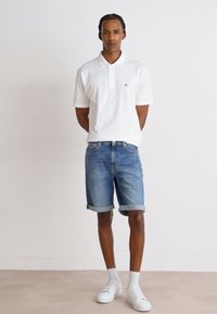 Vit polotröja, blå denimshorts med upprullade fållar, vita strumpor och sneakers. Enkelt mönster, avslappnad passform och släta texturer.