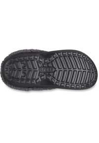 Suela de goma negra con un patrón texturizado. El borde superior presenta un material suave similar a la piel de un animal en color gris, otorgando una apariencia acogedora y cálida.