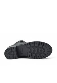 Suela de bota negra con surcos profundos y patrón en zigzag. El material parece goma con una superficie texturizada. Tacón plano, bordes suaves.