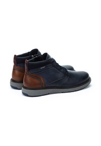 Zapatos de cuero azul marino con acentos marrones, diseño de media caña, cierre de cordones en la parte frontal y suela de goma texturizada gris; detalles de costura en los laterales.