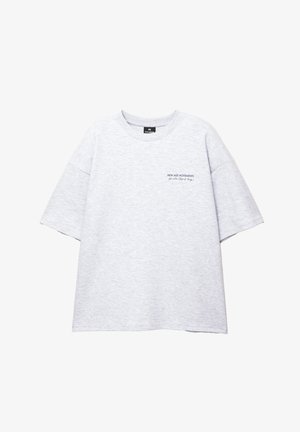 Grijze oversized t-shirt van katoen, met een ronde hals en korte mouwen. "NEW AGE MOVEMENTS" gedrukt in donkere letters op de borst.