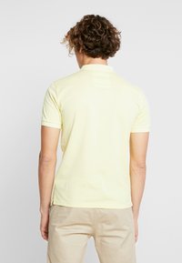 Polo giallo a maniche corte con fessure laterali. Realizzato in tessuto morbido, presenta un colletto e un piccolo etichetta sul retro.