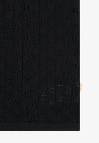 Tissu tricoté noir présentant un motif texturé avec des détails ajourés et des rayures verticales. Une petite étiquette est visible sur le bord.