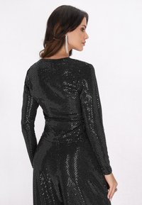 Schwarzes Paillettenkleid mit langen Ärmeln und taillierter Passform, ausgestattet mit einer glatten Textur und einem runden Ausschnitt, der schimmernde Details zeigt.