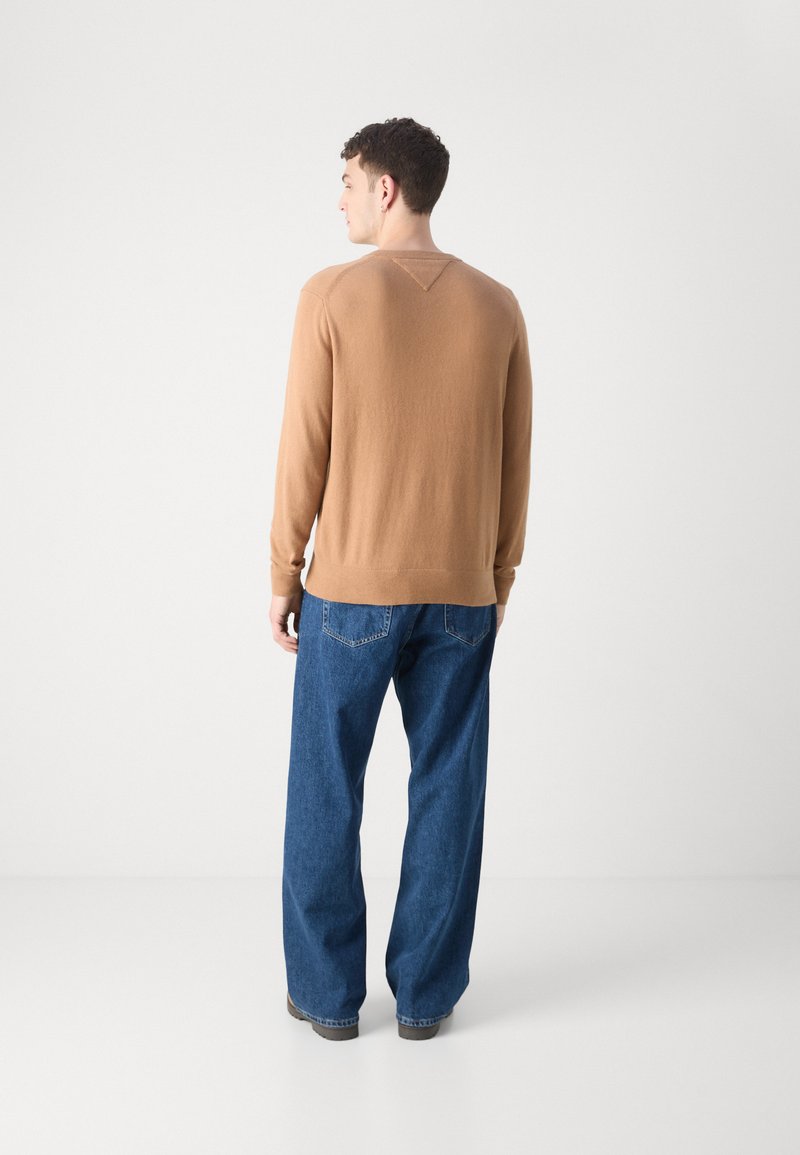 Maglione marrone a maglia con dettagli a V sul retro, abbinato a jeans in denim blu larghi. L'outfit ha una vestibilità comoda e una texture morbida.