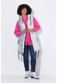 Iridescente, gewatteerde vest met een capuchon, zwarte ritsen en koordjes. Draag het over een roze, lange mouwen shirt. Blauwe jeans en glanzende zilveren enkellaarsjes.