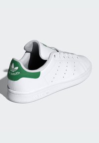 Hvit lær sneakers med grønne detaljer på hælen, perforerte sideelementer, rund tå og flat gummisåle. Klassisk design.