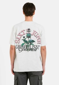 Camiseta de manga corta gris claro con un gráfico floral vibrante y el texto “SIXTH JUNE GROWTH ISN'T Optional” en rosa y negro.