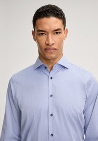 Camicia button-up azzurro chiaro con una sottile texture, maniche lunghe e colletto a punta. Presenta bottoni scuri lungo la parte frontale.