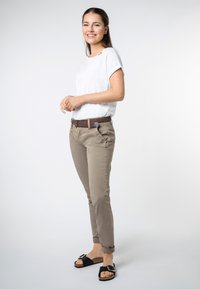 Witte shirt met korte mouwen, beige slim-fit broek, bruine gevlochten riem en zwarte sandalen met een zilveren gesp. Soepele stof, opgerolde broekspijpen.